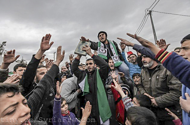 Syrian refugees in a camp in Turkey proclaim their reverence for the Koran being held aloft, and their hatred for Syrian dictator Hafez Assad. (Photo by Freedom House/Flickr) 